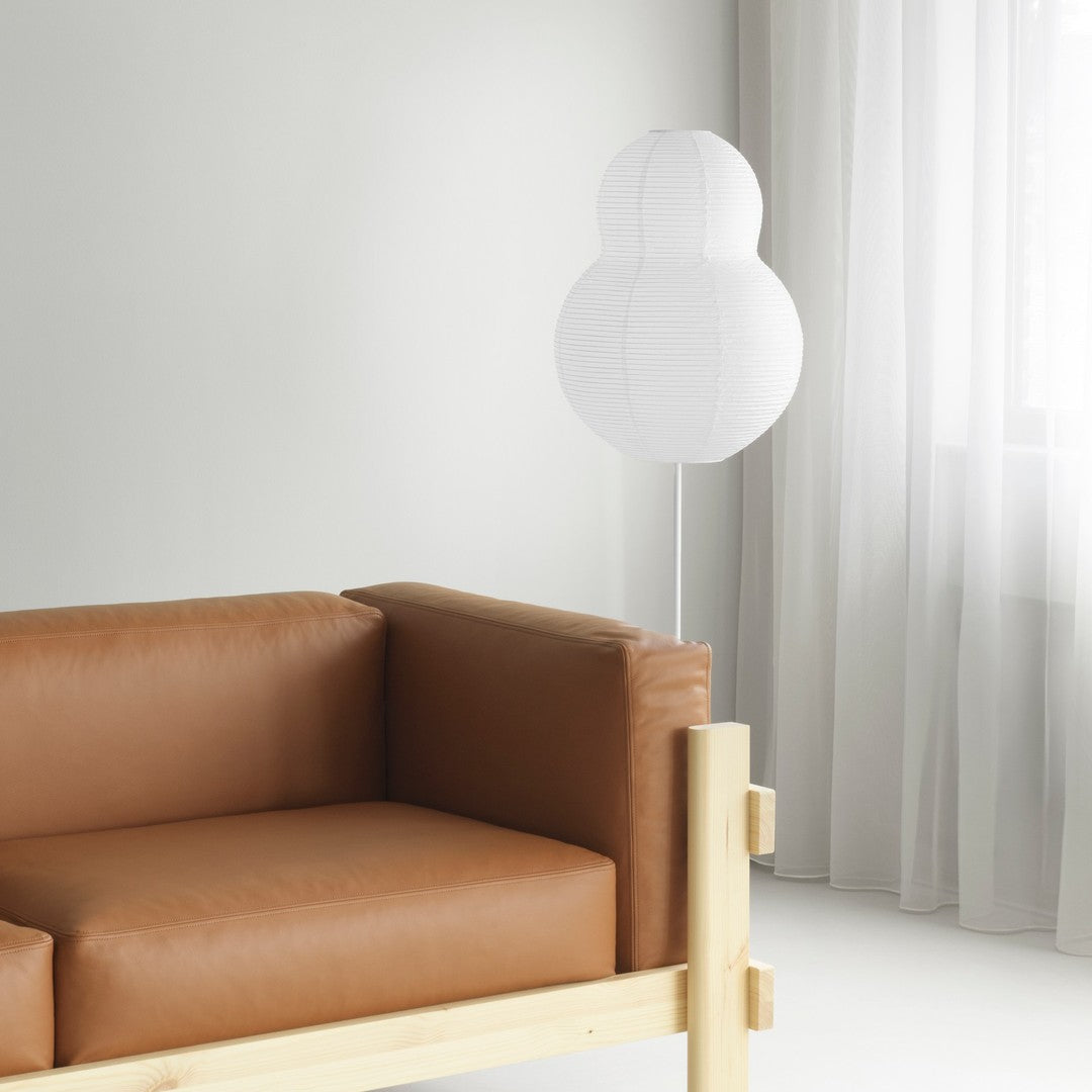 Brown leather sofa against a light gray wall with a white lamp and sheer curtains, creating a modern, minimalist vibe.
