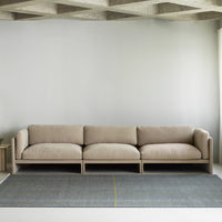 Beige modern sofa on a gray rug with subtle yellow lines against a minimalist backdrop. 