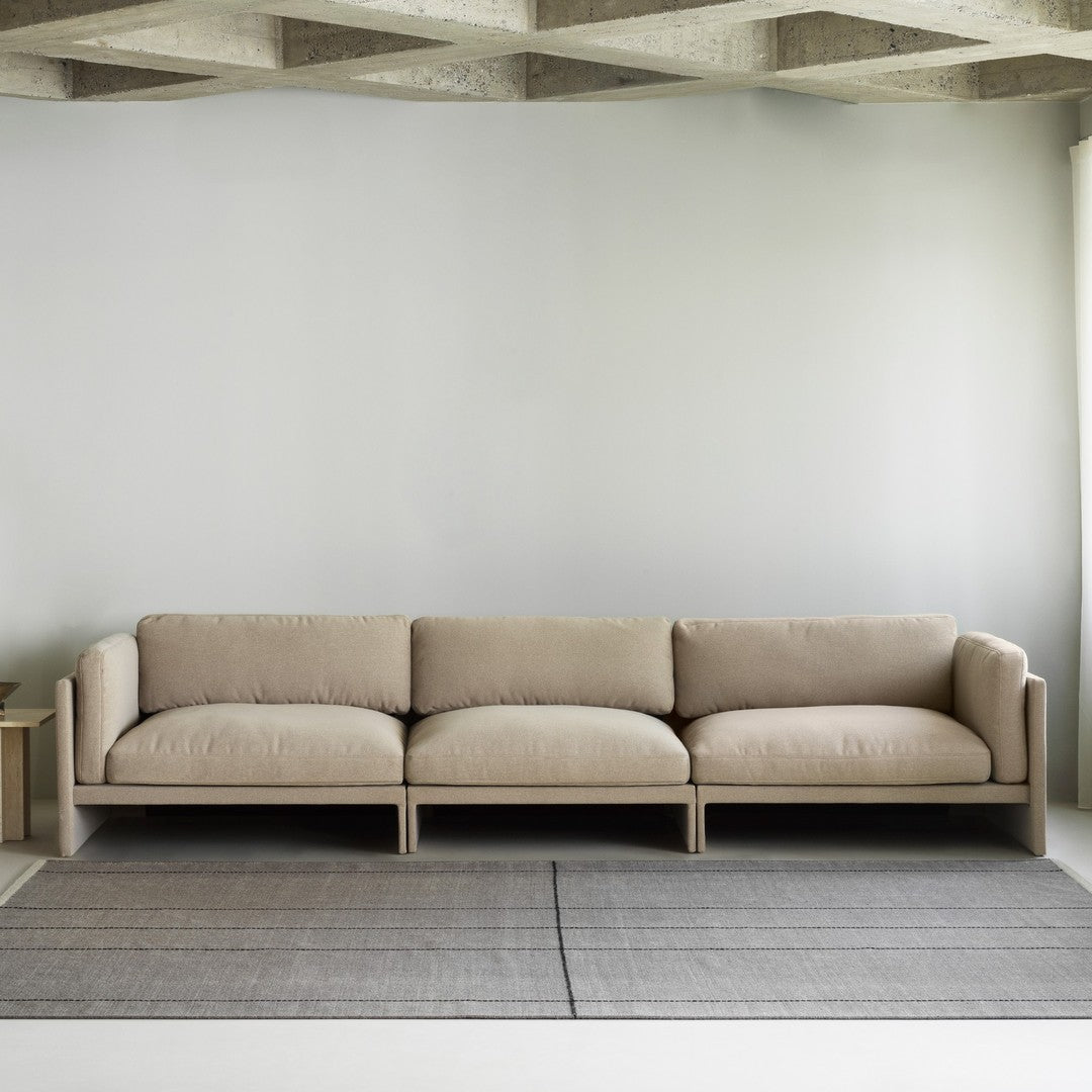 Beige modern sofa with clean lines, featuring soft upholstery and a minimalist gray rug with subtle stripes.