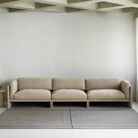 Beige modern sofa with clean lines, featuring soft upholstery and a minimalist gray rug with subtle stripes.
