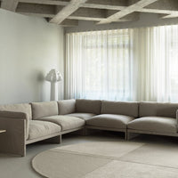 "Beige sectional sofa with textured fabric, paired with a soft circular cream rug and light sheer curtains."