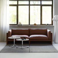 Brown leather sofa with gray striped rug and soft white curtains, enhancing a modern, minimalist aesthetic.