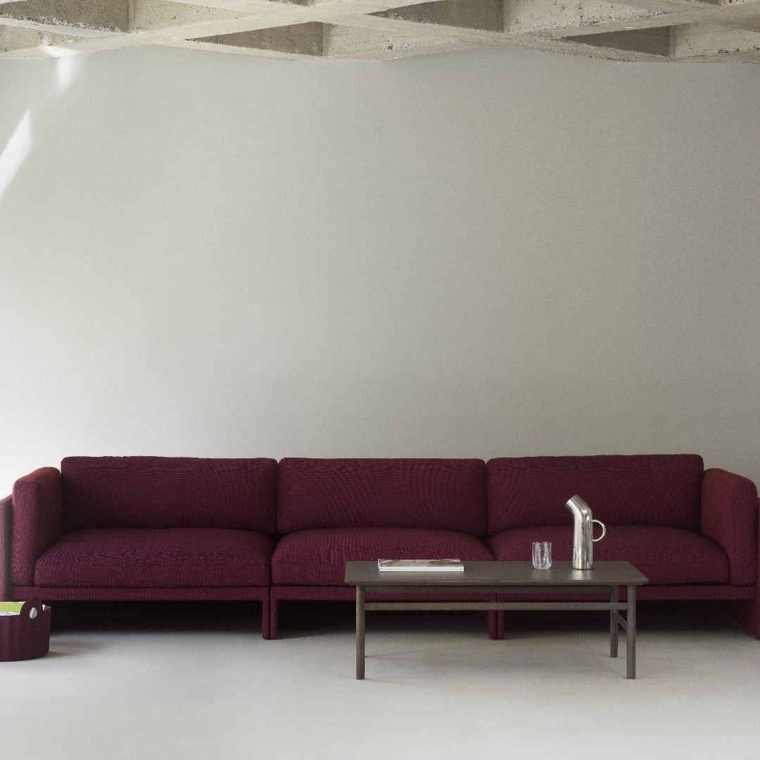 Burgundy textured sofa with muted gray wall and minimalist wooden coffee table. Modern, sleek design in subtle tones.