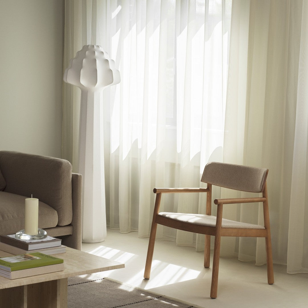 Light beige fabric chair with wooden frame, surrounded by soft cream curtains and neutral-toned decor.