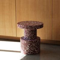 Round maroon table with a speckled white pattern, featuring a cylindrical base and minimalist design.