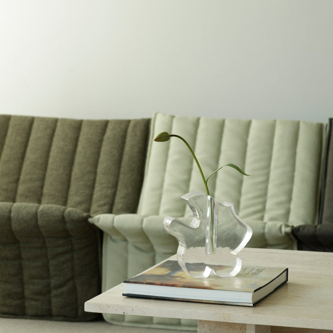 Green and beige ribbed sofas with a clear vase on a light table, creating a minimalist, contemporary aesthetic.