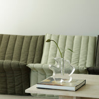 Green and beige ribbed sofas with a clear vase on a light table, creating a minimalist, contemporary aesthetic.