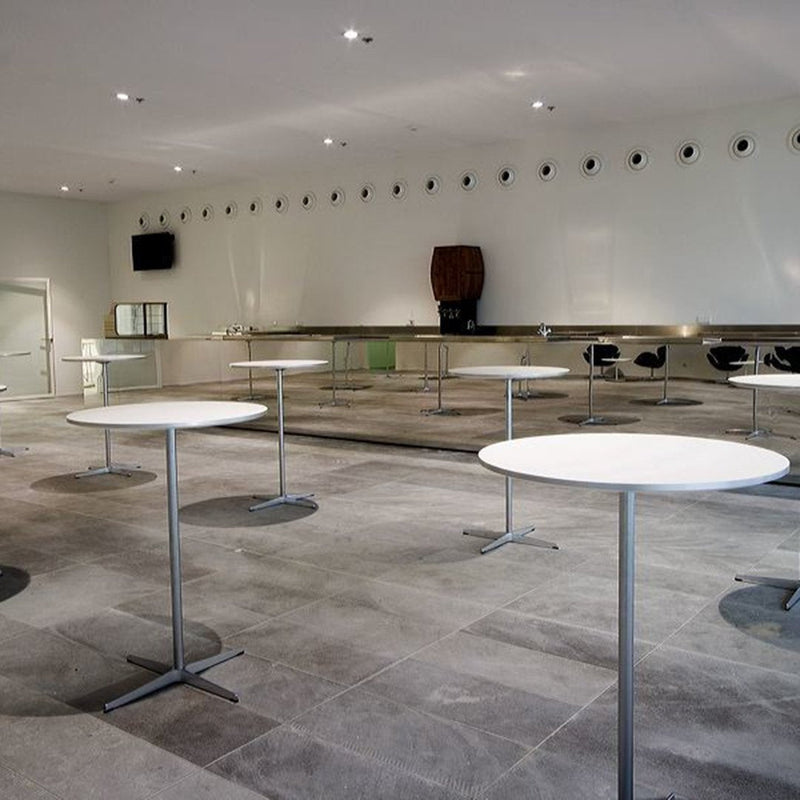 "Modern white round tables on gray stone floor in a minimalist venue with neutral walls and sleek lighting."