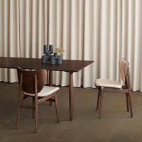 Elegant brown wooden dining table and chairs with neutral fabric cushions, set against soft beige curtains.