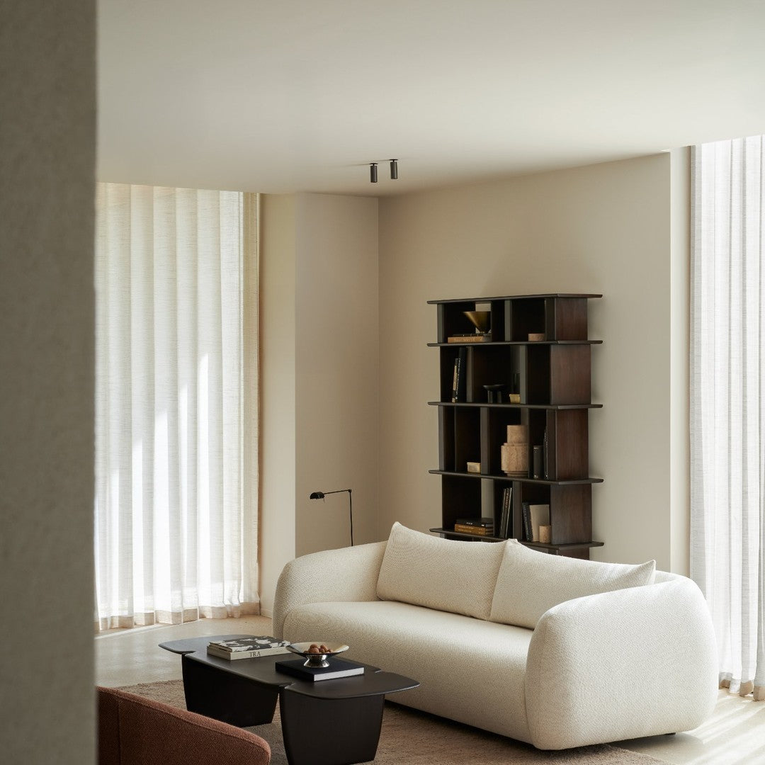Cozy white textured sofa against neutral walls, complemented by dark wooden shelves and light curtains. Elegant minimalist design.