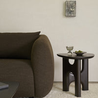 Brown textured sofa with a curved armrest beside a sleek dark wood side table, creating a modern minimalist look.
