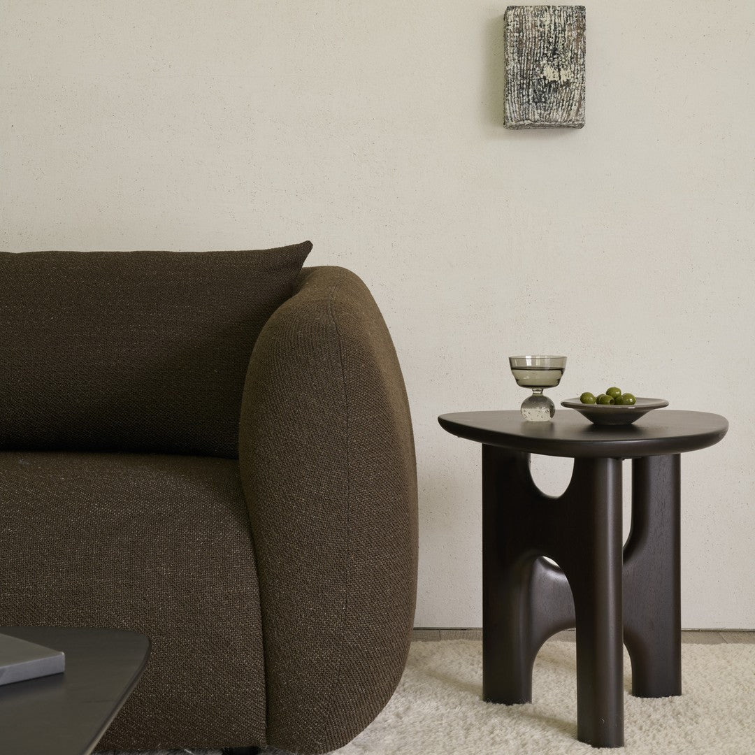 Brown textured sofa with a rounded arm, alongside a sleek black side table and minimalist decor.