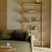 Elegant green sofa with dark accent pillows and natural wood shelf showcasing neutral decor in warm, soft tones.