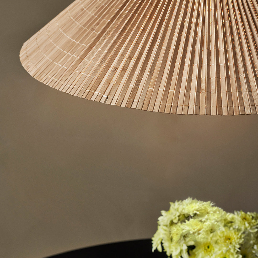 Beige pleated lampshade with a textured pattern, complementing a dark base and soft green floral arrangement.