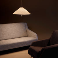 Gray textured sofa and dark upholstered armchair under a warm beige pendant light against a dark background.