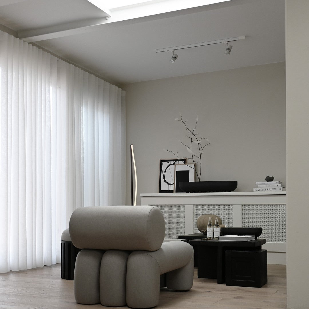 Stylish gray fabric chair with smooth curves, complemented by black accent tables and white sheer curtains.