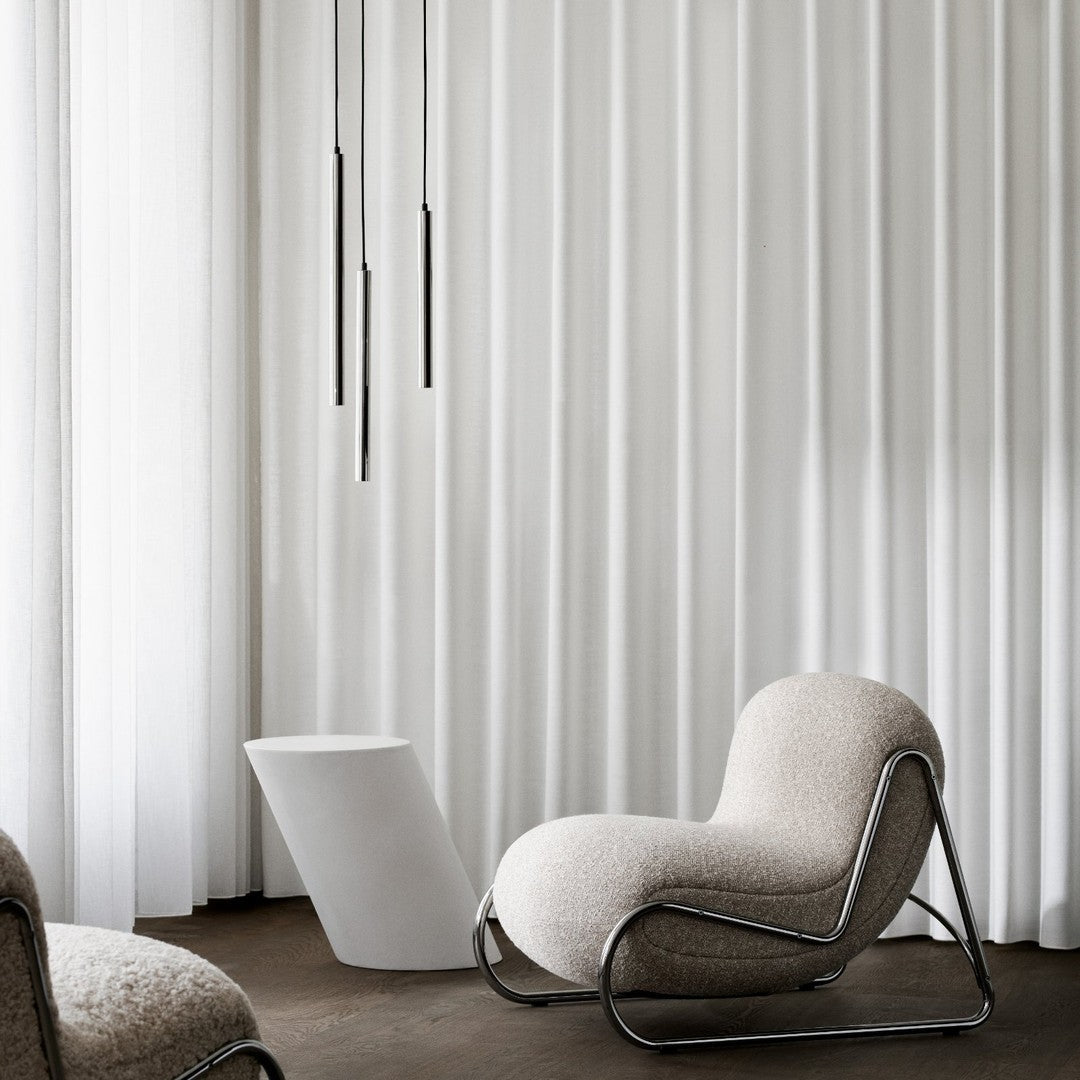 Soft beige chair with sleek chrome accents, surrounded by crisp white curtains in a minimalist setting.