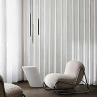 Soft beige chair with sleek chrome accents, surrounded by crisp white curtains in a minimalist setting.