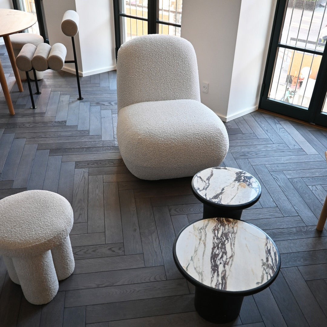 Modern furniture featuring soft white texture, round marble tabletops with gray and gold veining, and dark wood flooring.