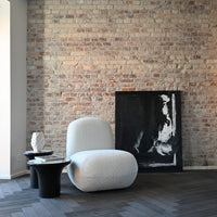 Textured white chair against a rustic brick wall, with black and white abstract artwork and dark wooden accents.