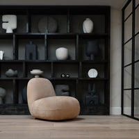Beige modern chair against a dark wood shelf, featuring various black and white decorative objects.