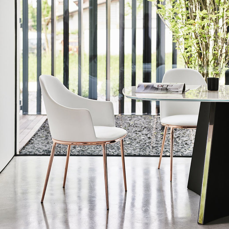 White chair with sleek design, soft upholstery, and rose gold legs against a modern indoor setting with striped windows.