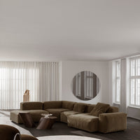 "Modern beige sectional sofa with soft, textured fabric in a minimalist room featuring white curtains and earthy tones."