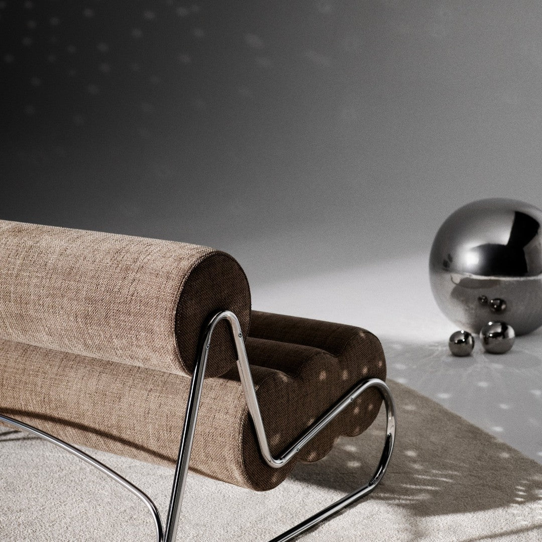 Brown textured fabric lounge chair with a sleek chrome frame and silver decorative orbs in a minimalist setting.