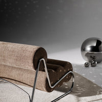 Brown textured fabric lounge chair with a sleek chrome frame and silver decorative orbs in a minimalist setting.