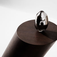 Silver and black glass vase atop a dark wood pedestal against a minimalistic white background.