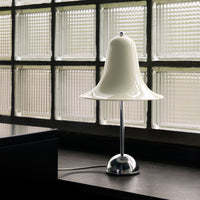 White bell-shaped lamp with a shiny chrome base, set against textured glass block background. Modern design element.