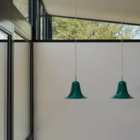 Two green bell-shaped pendant lights hanging against a minimalist interior with a white backdrop and large windows.