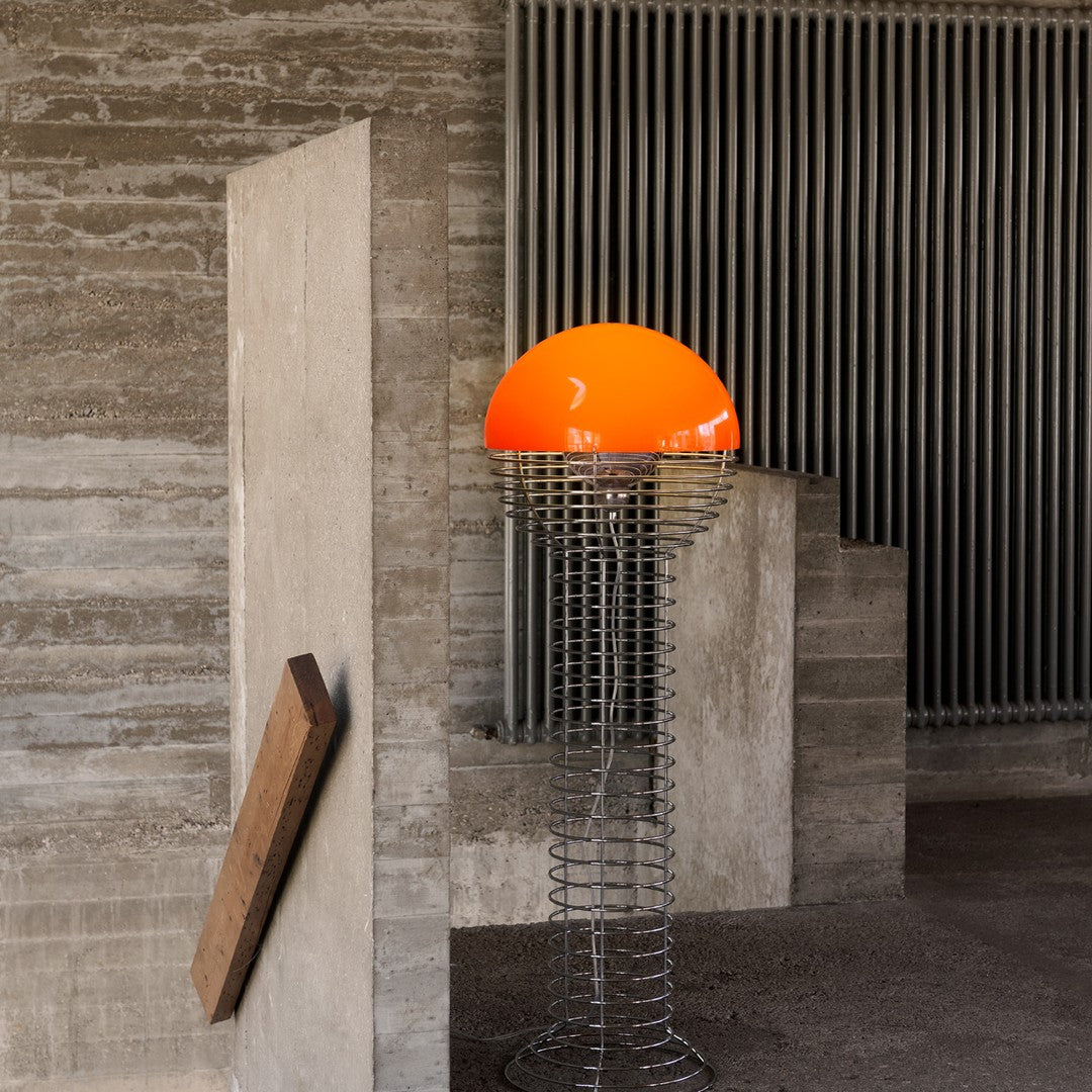 Modern lamp with a vibrant orange dome and sleek metallic wire base, set against a neutral textured background.
