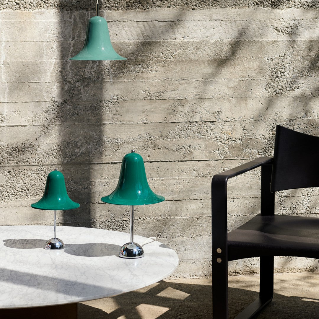 Green bell-shaped lamps with glossy finish on a marble table, set against a minimalist concrete wall.