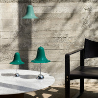 Green bell-shaped lamps with glossy finish on a marble table, set against a minimalist concrete wall.