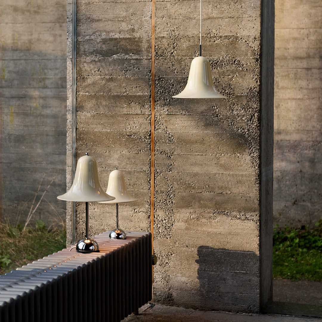 Cream-hued pendant and table lamps with sleek chrome bases against a textured concrete backdrop.