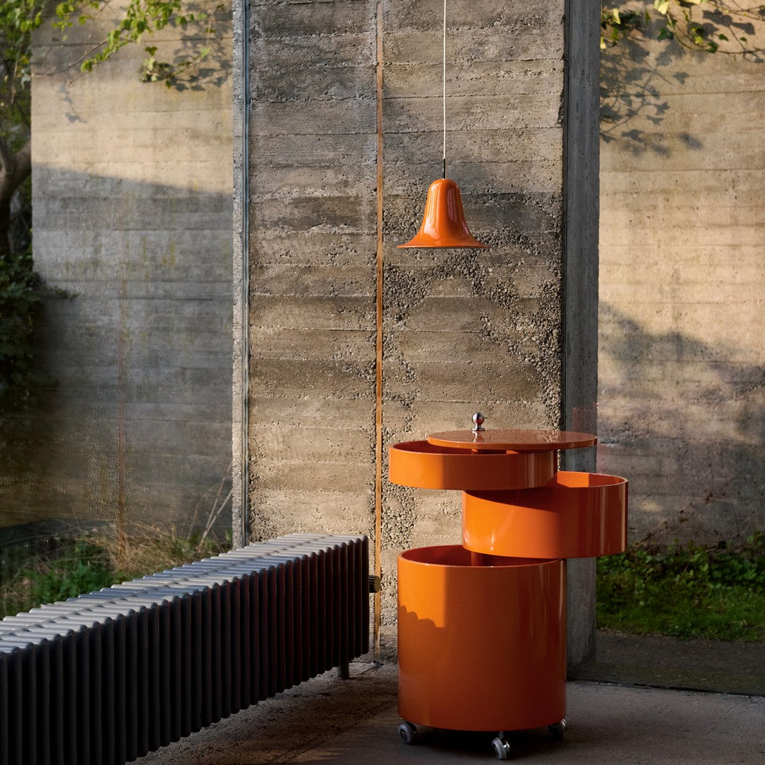 Modern orange mobile bar cart with sleek lines, paired with an orange pendant light, against a concrete backdrop.