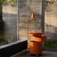 Modern orange mobile bar cart with sleek lines, paired with an orange pendant light, against a concrete backdrop.