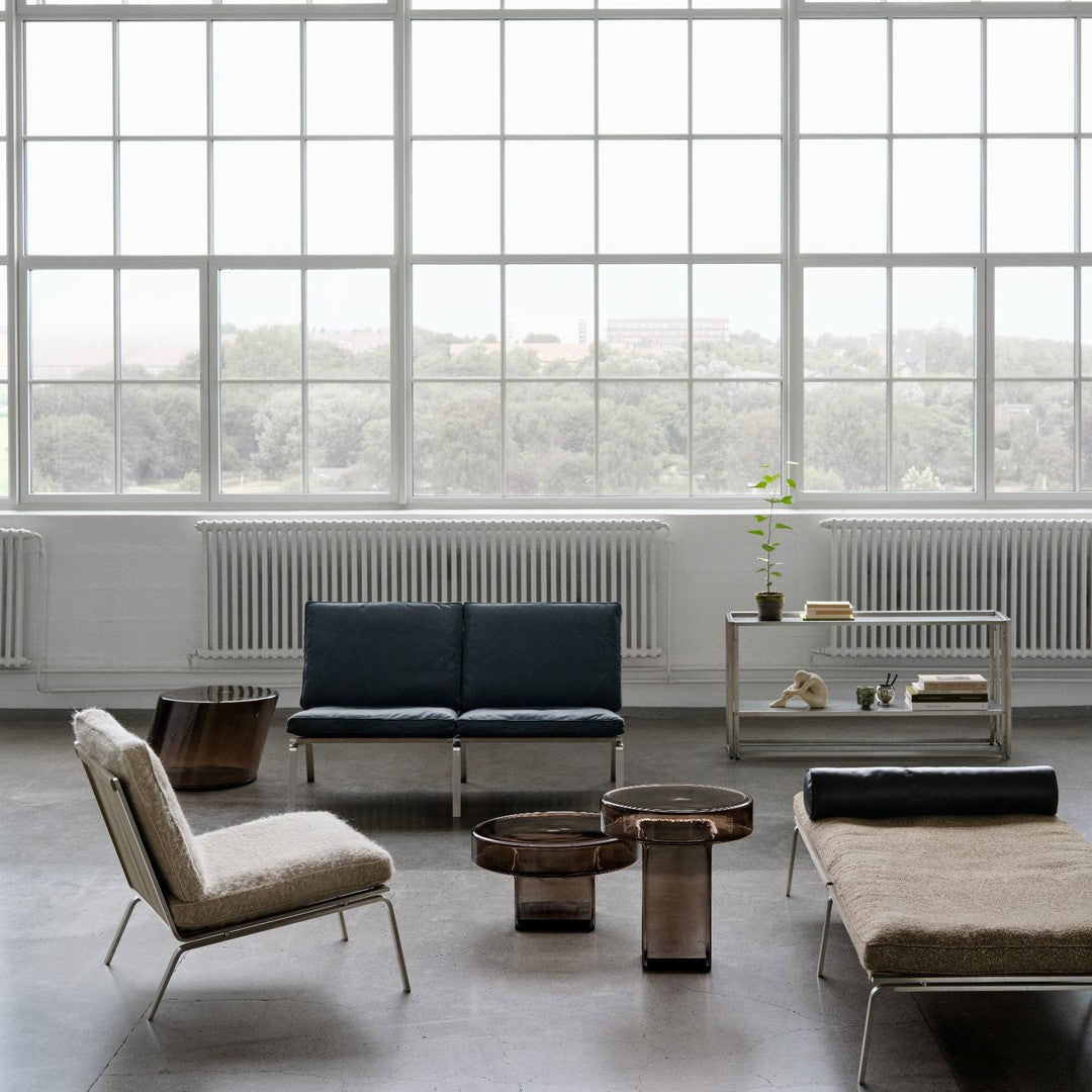 Modern furniture in muted tones: navy blue, natural beige, and metallic bronze accents on a light concrete floor.