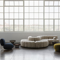Beige curved sofa with soft pleats, complemented by a deep blue chair and green accent table in a modern space.