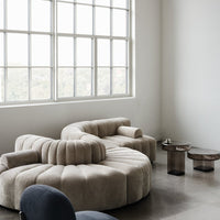 Beige curved sofa with plush texture, complemented by dark glass accent tables, in a bright minimalist room.
