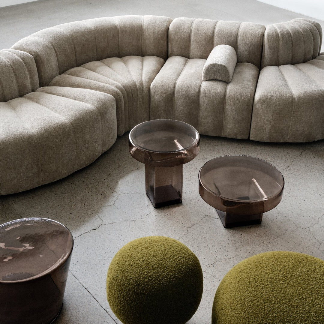 Beige curved sofa with ribbed texture, paired with glossy brown glass tables and vibrant green round poufs.