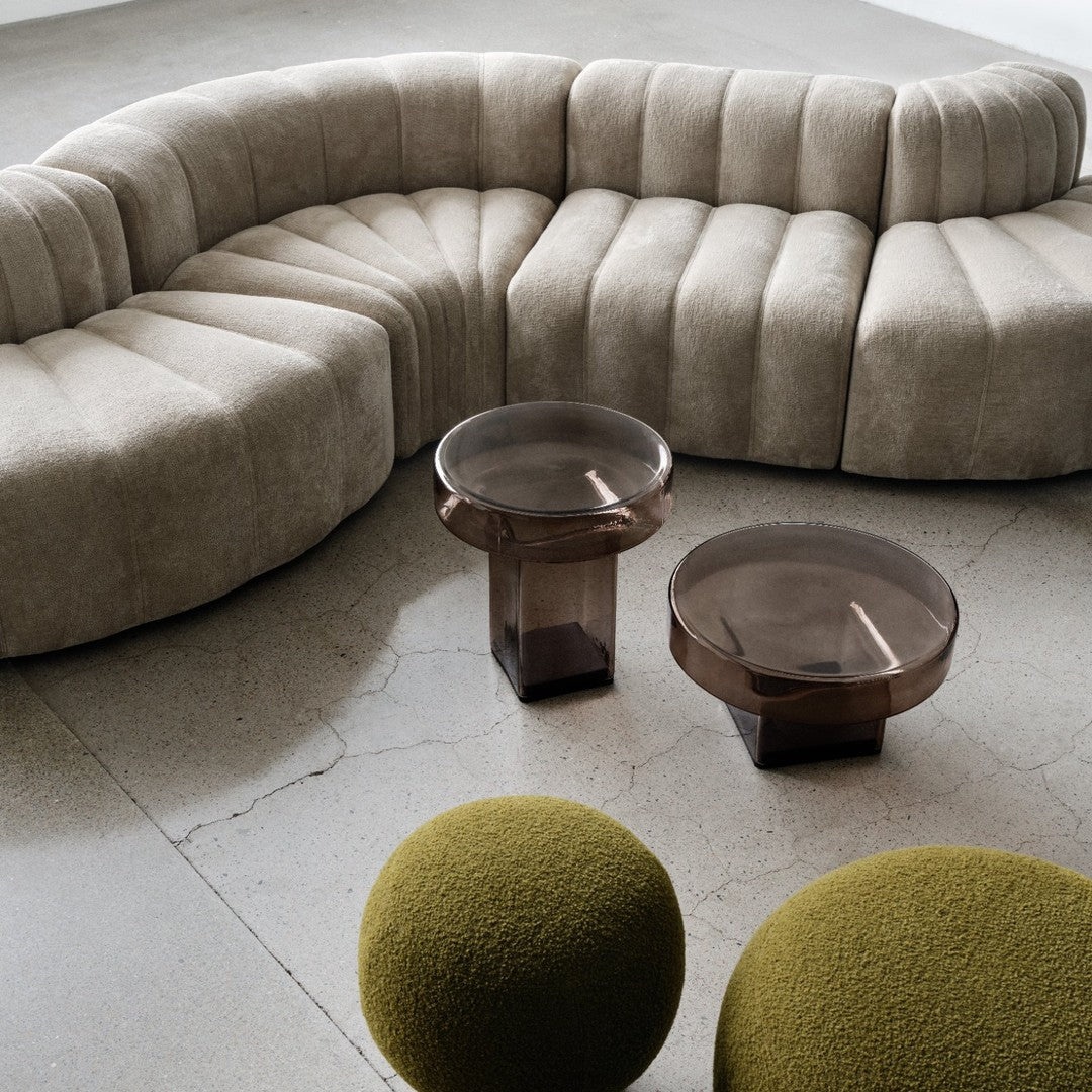 Beige curved sofa with pleated pattern, paired with round brown glass tables and green textured ottomans.