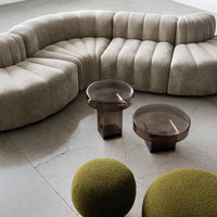 Beige curved sofa with pleated pattern, paired with round brown glass tables and green textured ottomans.