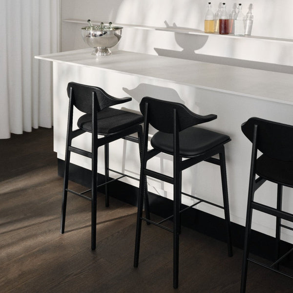Sleek black bar stools against a minimalist white countertop, accentuated by warm wood tones and soft shadows.