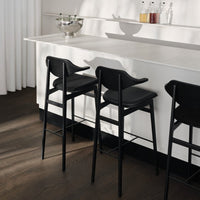 Black bar stools with sleek lines against a minimalist white countertop and warm wood flooring.