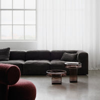 Modern living room with a dark gray sofa and burgundy accent chair, featuring clear and smoky glass tables.