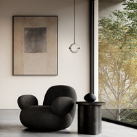 Black textured chair, muted beige wall art, and sleek black lighting in a modern, minimalistic interior setting.
