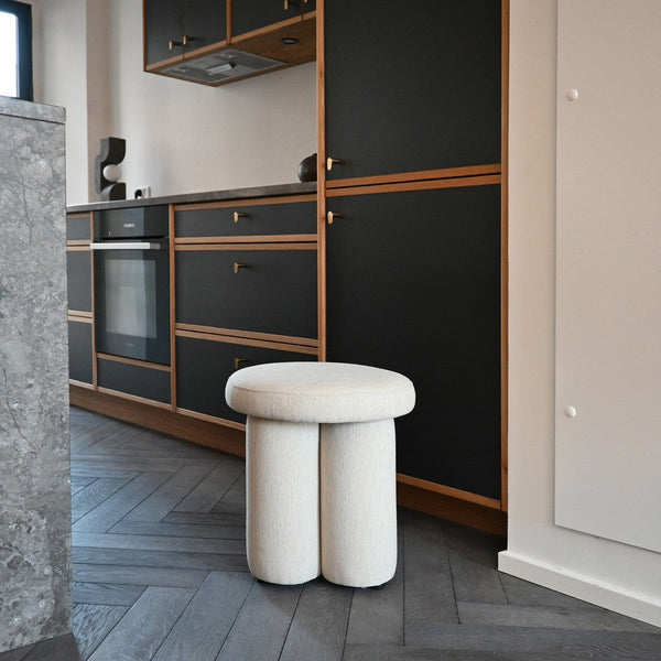 Cream-colored round stool with a textured pattern, set against dark wood and cabinets for a modern contrast.