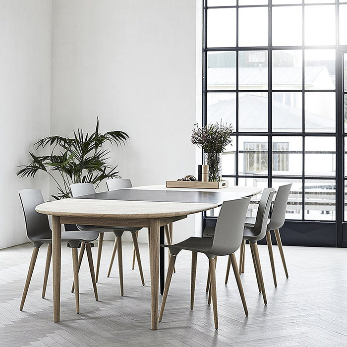 Light grey round dining table with natural wood accents, surrounded by sleek grey chairs against a bright, airy backdrop.